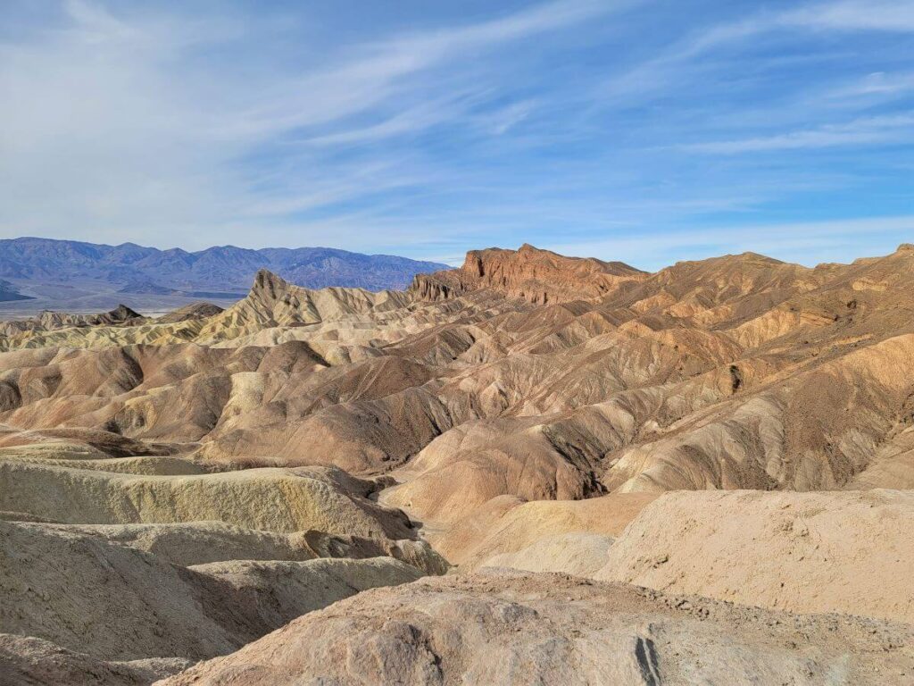Golden rocky hiills under a blue sky at Death Valley National Park in California is on this list of u s national parks