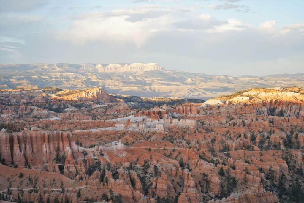 This one day in Bryce Canyon National Park itinerary includes view like this one, with a landscape full of orange hills and rock spires is dotted with evergreen trees under a sunset sky.