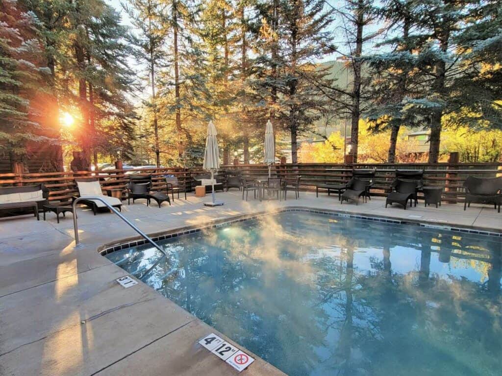 A pool pool steaming as the sun rises between trees in the background.