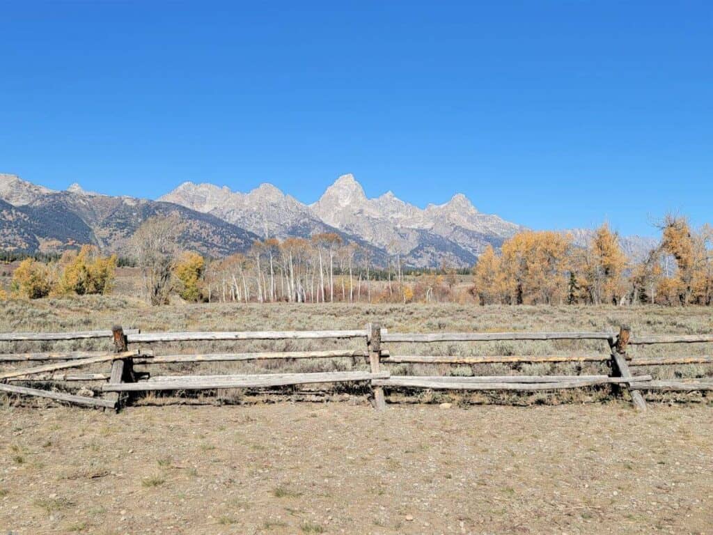A wooden fence with a field and a row of mountains behind it.
