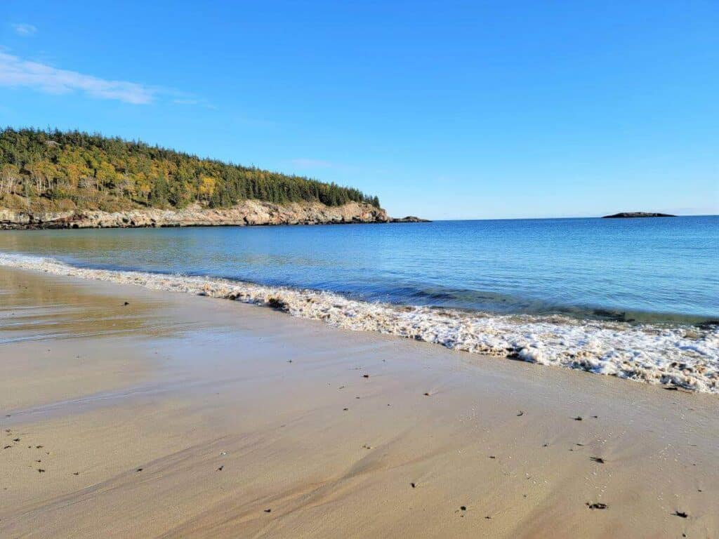 A sandy beach in Acadia National Park with a wave washing ashore.